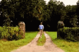 a man in a blue shirt is walking down a dirt road .