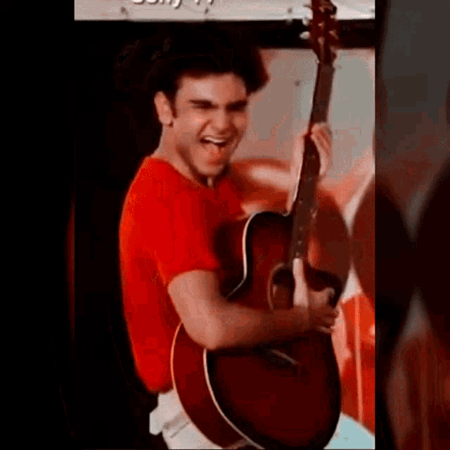 a man in a red shirt is holding a red guitar and laughing .
