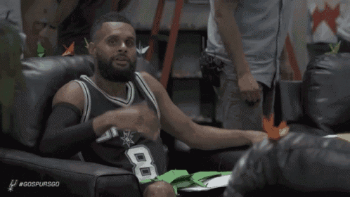 a man in a spurs jersey is sitting in a chair and making a funny face .
