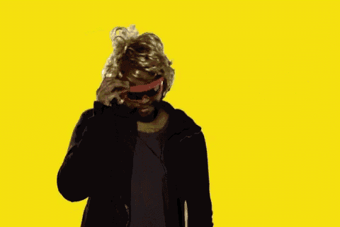 a man wearing sunglasses and a wig is talking on a cell phone with the word sup written on the yellow background .