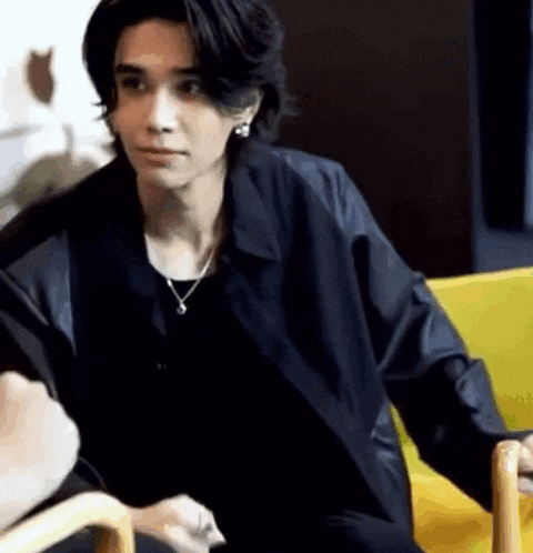 a young man is sitting on a yellow chair wearing a black jacket .