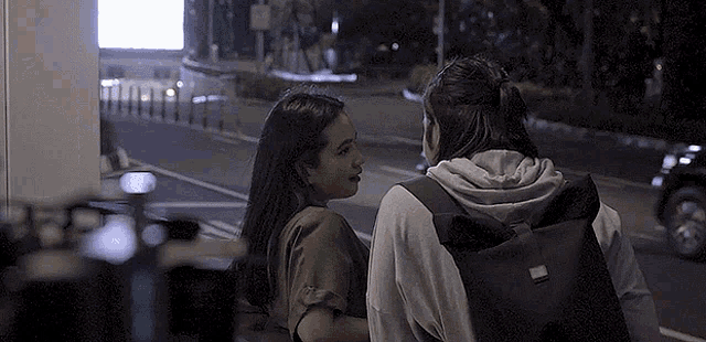 a couple of women standing next to each other on a street at night .