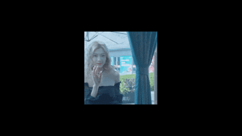 a woman in a black off the shoulder top looks out of a window