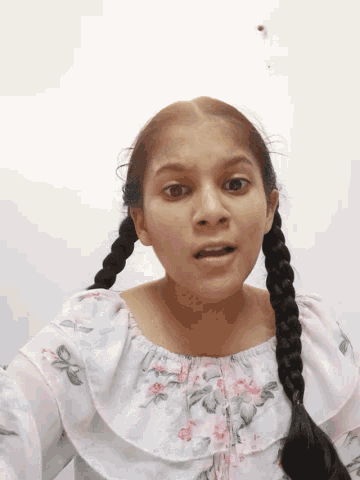 a girl with braids is wearing a white floral shirt