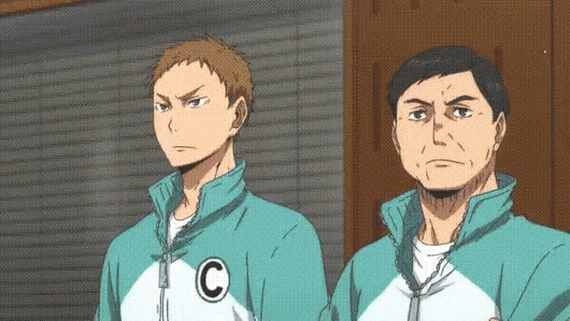 two men are standing next to each other in front of a brick wall and looking at something .