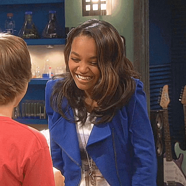a woman in a blue jacket smiles while standing next to a boy in a red shirt
