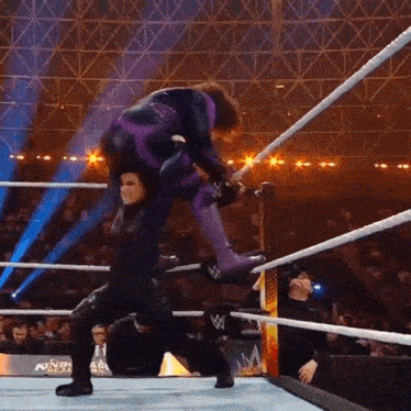 a wrestler in a purple suit is carrying another wrestler in a wrestling ring .
