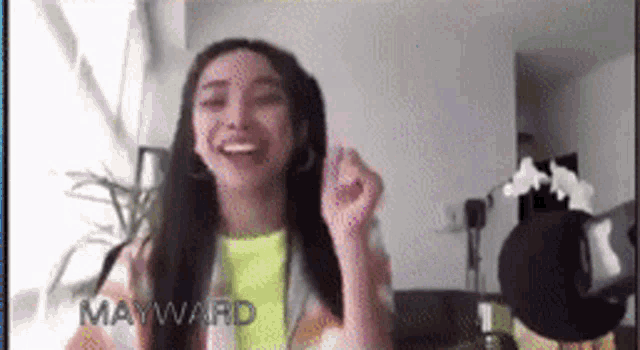 a woman is laughing and making a heart shape with her hands while sitting in a living room .