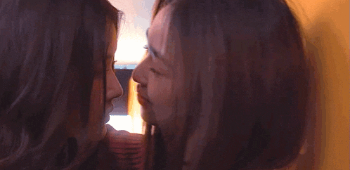 a couple of women are kissing each other in front of a yellow wall