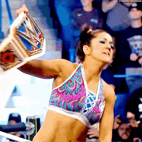 a woman in a colorful top is holding a wrestling belt