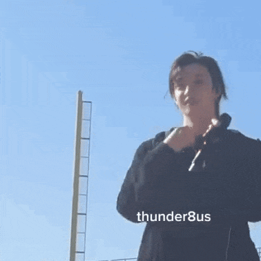 a man in a black jacket is holding a microphone in front of a blue sky .