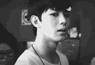 a black and white photo of a young man with a necklace around his neck .