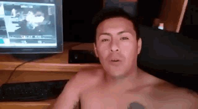 a man without a shirt is sitting in front of a computer screen .