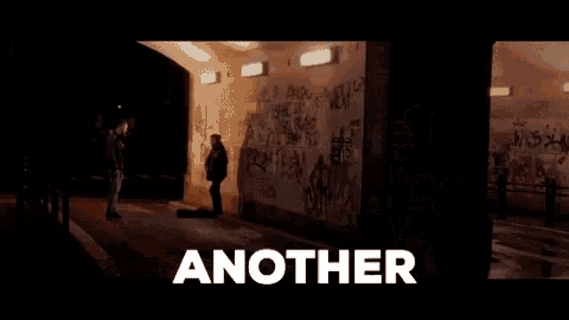 a man in a leather jacket is standing in front of a graffiti covered wall .