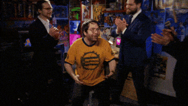 a man wearing a yellow shirt that says eclipse stands in a room with other men