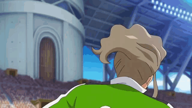 a man in a green jacket is standing in front of a stadium with a large building in the background .