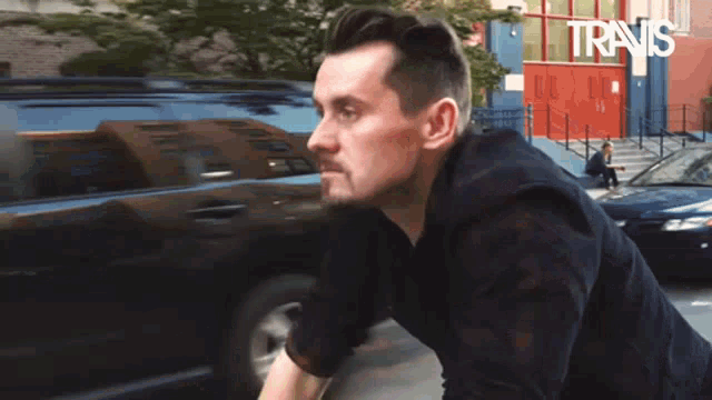 a man in a black shirt is standing in front of a car with the words travis written on the bottom