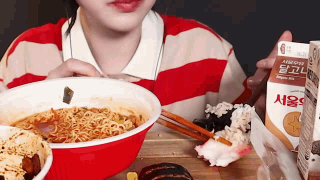 a woman in a red and white striped shirt is eating a bowl of noodles and drinking milk .