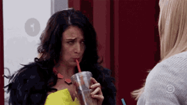 a woman is drinking a drink through a straw while standing next to another woman .