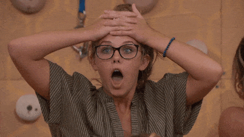 a woman wearing glasses is covering her face with her hands in front of a climbing wall