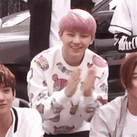 a young man with pink hair is clapping his hands while sitting next to a group of young men .