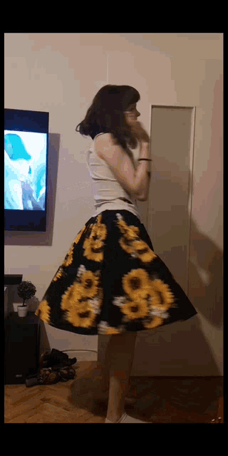 a woman wearing a sunflower skirt is standing in front of a television