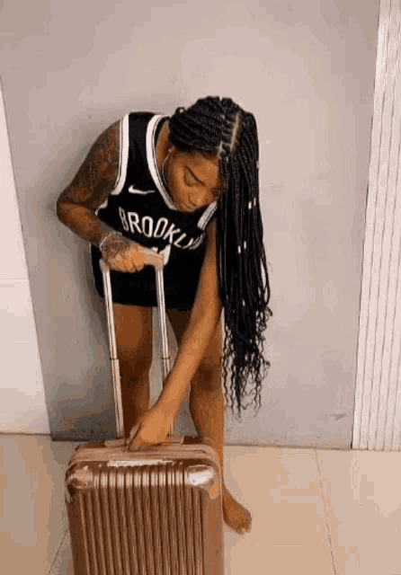 a woman wearing a brooklyn nets jersey is holding a suitcase .