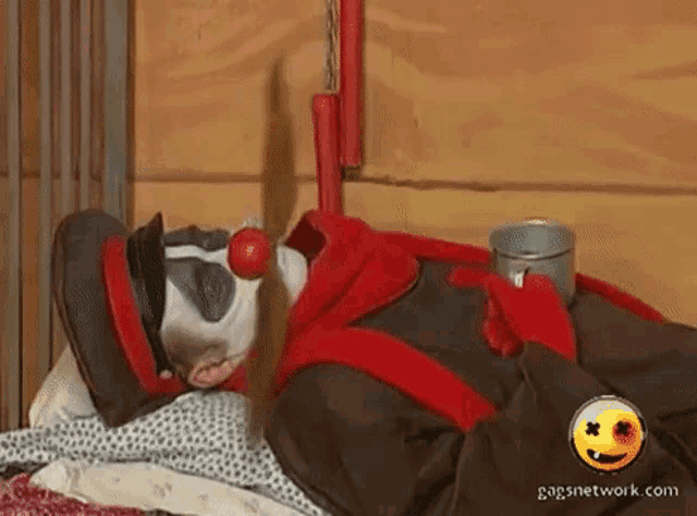 a clown with a red nose is laying on a bed with a gagsnetwork.com logo