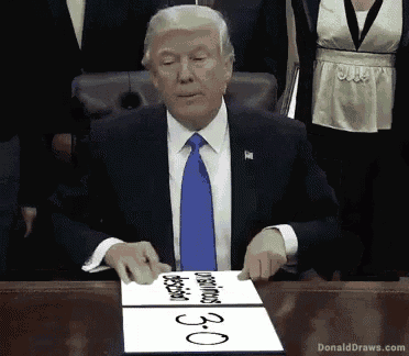 donald trump is sitting at a desk with a piece of paper that says " obama " on it