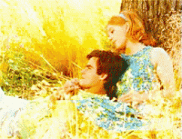 a man and woman are sitting under a tree in a field of flowers