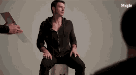 a man is sitting on a stool while a man holds a piece of paper in front of him .