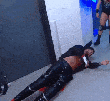 a wrestler is laying on the floor while another wrestler stands behind him .