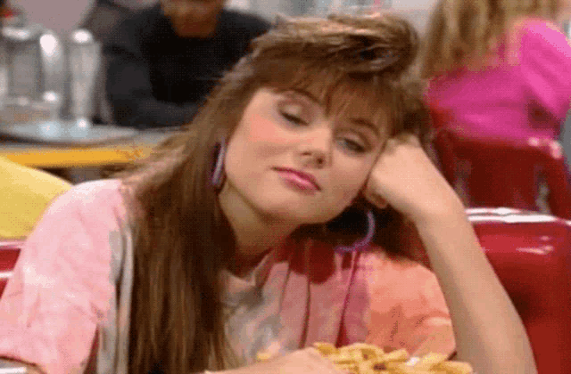 a woman in a pink shirt is sitting at a table with her head resting on her hand .