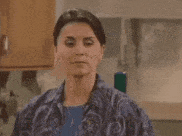 a woman is making a funny face in a kitchen while wearing a blue shirt .