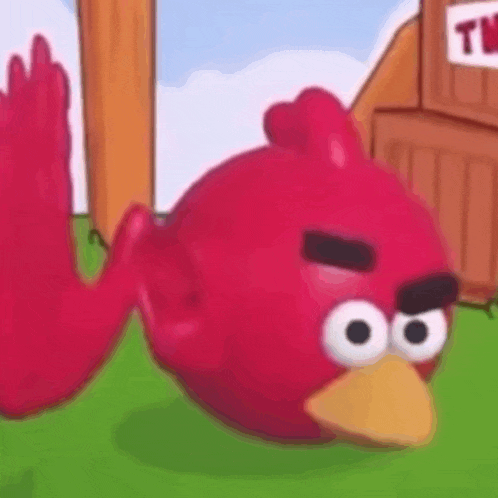 a red angry bird is laying on its back on the grass .