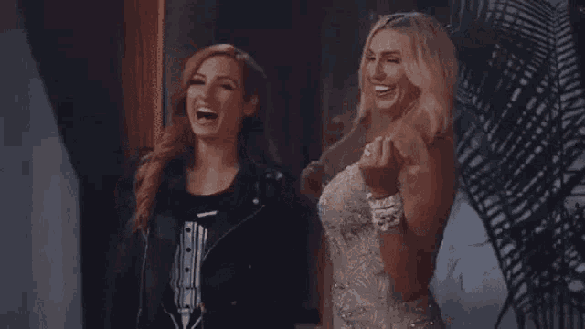 two women are standing next to each other in a room . one of the women is wearing a tuxedo .