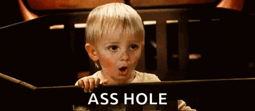a baby is sitting in a crib with the words `` ass hole '' written on the screen .