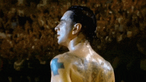 a shirtless man with tattoos on his back is standing in front of a crowd of people .