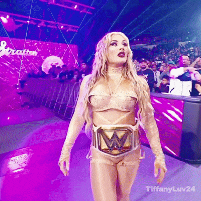 a woman in a wrestling costume with a w belt is walking on a stage .