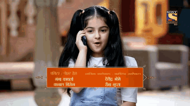 a little girl is talking on a cell phone with a sony television advertisement in the background