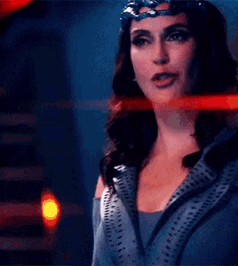 a woman wearing a mask and a crown is standing in a dark room .