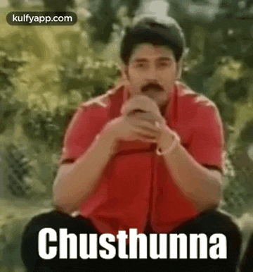 a man in a red shirt is sitting on a bench with his hands folded and the words chusthanna written on the screen .