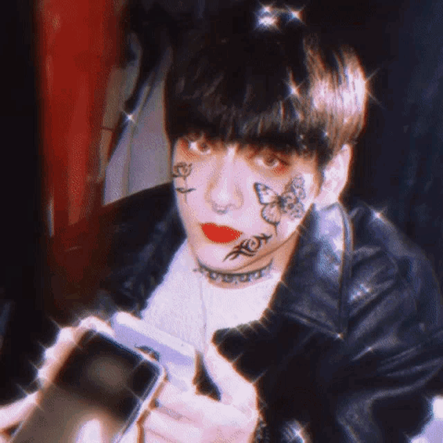 a young man with butterfly tattoos on his face is holding a cell phone .