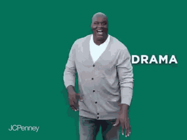 a man in a gray cardigan is standing in front of a green background and laughing .