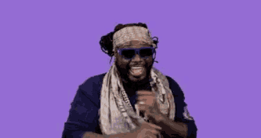 a man wearing sunglasses and a scarf is dancing against a purple background .