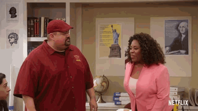 a man in a red shirt stands next to a woman in a pink jacket with a netflix logo on the bottom right