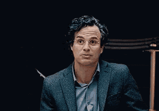 a man in a suit and blue shirt is making a funny face in a dark room .