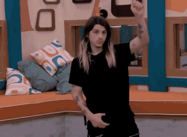 a man in a black shirt with a tattoo on his arm stands in front of a couch with colorful pillows on it