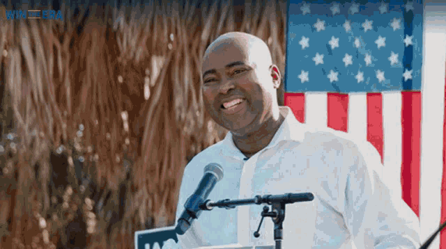 a man stands at a podium in front of a microphone with an american flag in the background
