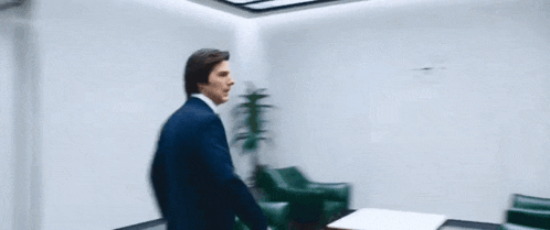 a man in a suit and tie is walking down a hallway in front of a clock .